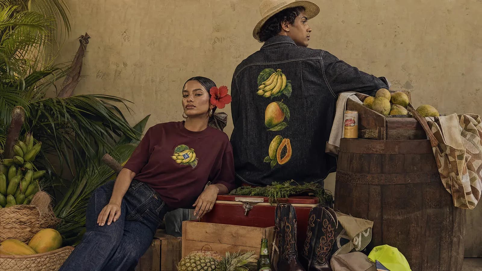 Dos figuras contra una pared de cal, con fruta y cajones