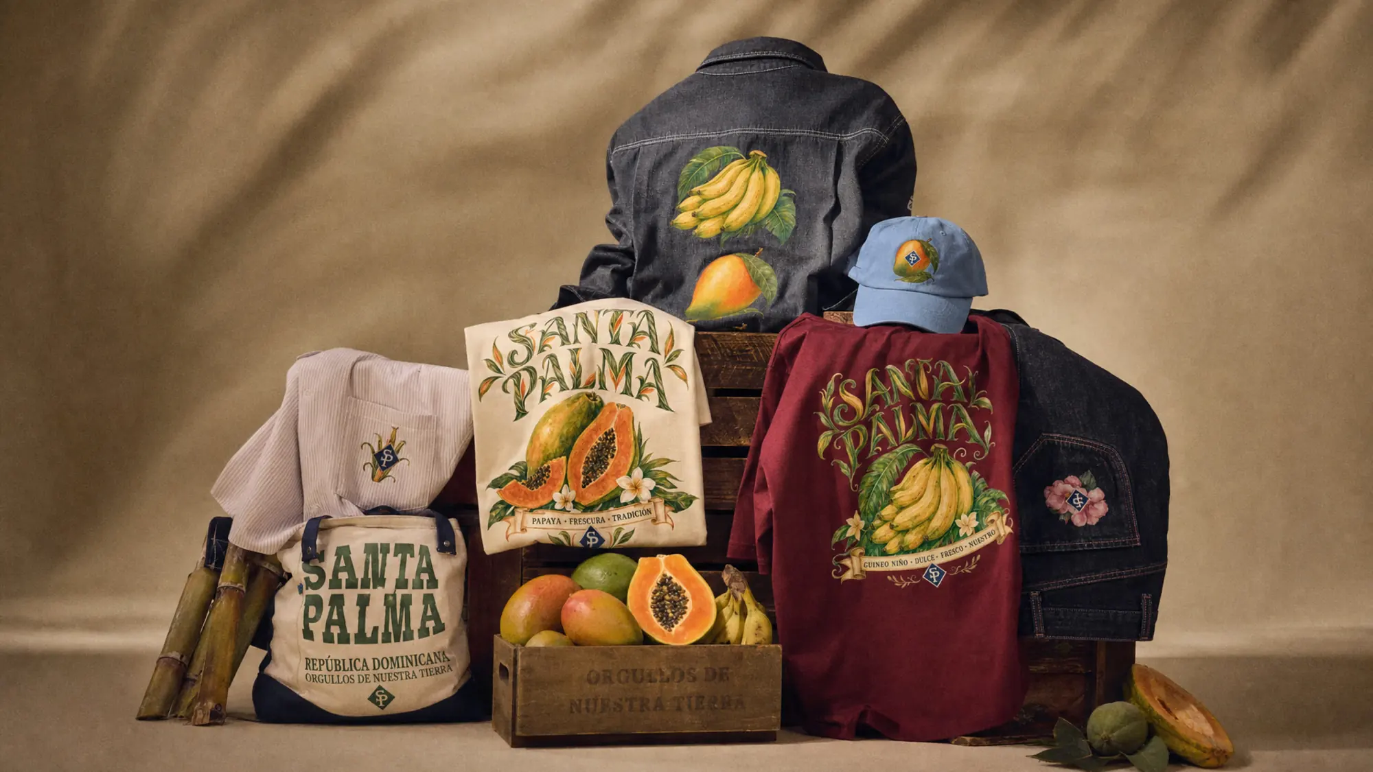 The Expression laid out on a crate: the fruit-print overshirt, the papaya tee, the wine guineo tee, a cap and the cosecha tote.